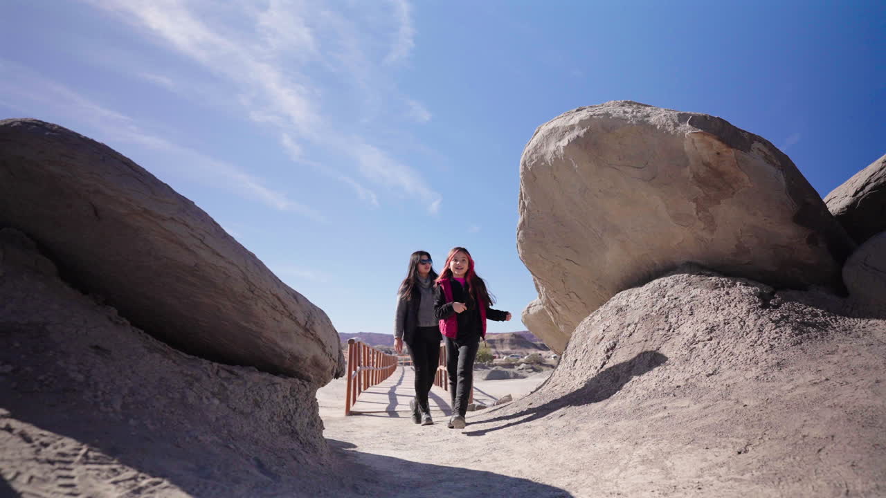 Wide-angle shot of mother and daughter exploring dramatic rock formations of Ischigualasto Moon Valley in Argentina, family travel