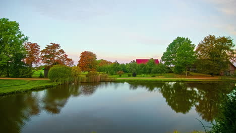 Lago-En-Un-Paisaje-Verde-Bucólico-E-Idílico-Con-Techo-Rojo-En-El-Fondo