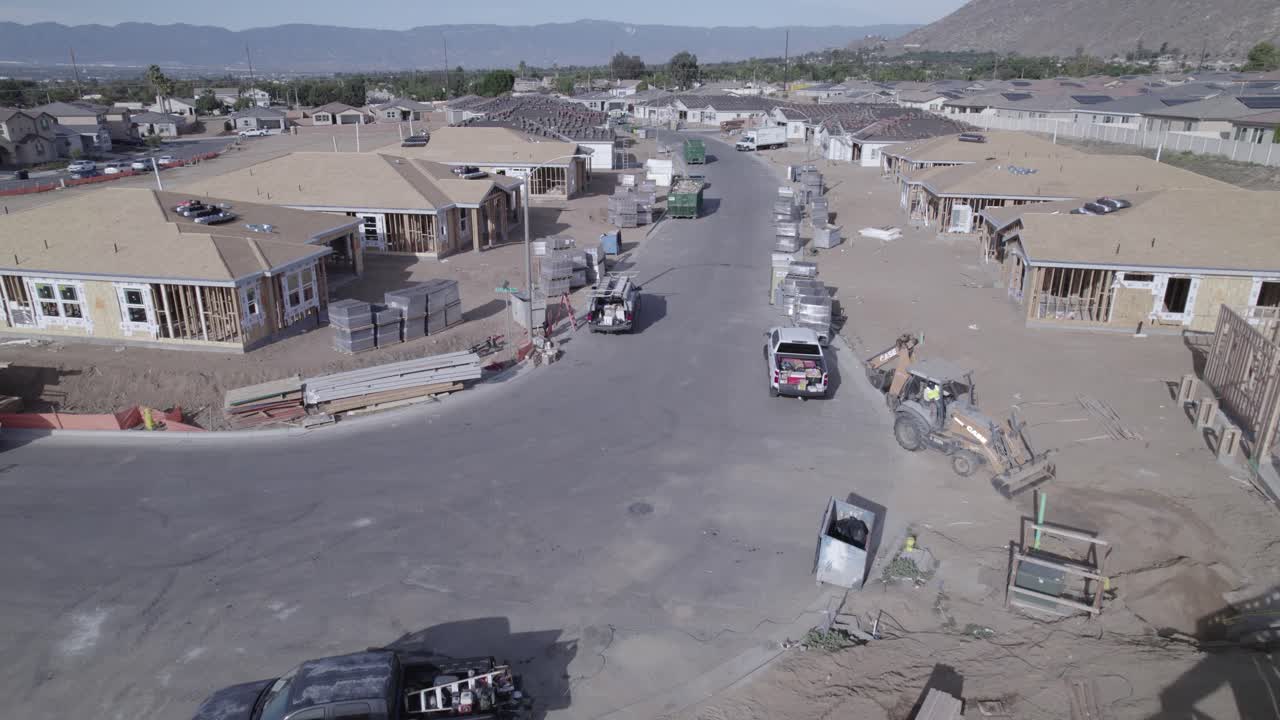 A drone smoothly flies by a home construction site, showcasing the varying late stages of home completion