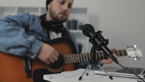 male musician singing and playing guitar, recording a song at home