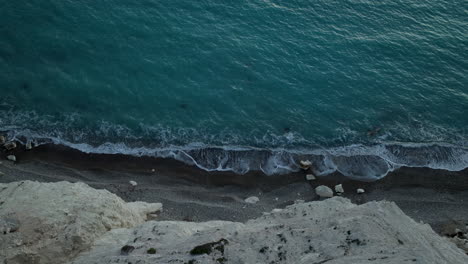 calm waves rolls over steep cliffy aphrodite's rock beach at twilight in kouklia, cyprus - aerial top down view