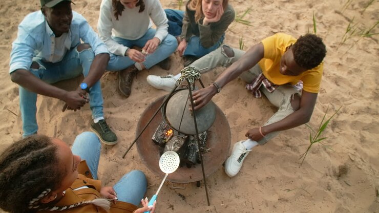 Friends Camping and Cooking Around a Campfire