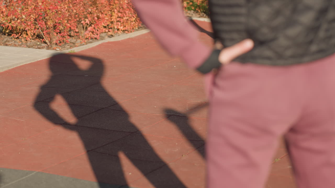 Back view of gym lover swaying waist sideways on outdoor rubber court under bright sunlight long shadows stretching across red mats, autumn shrubs lining background motion captured mid exercise