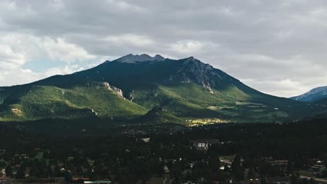 bright sunlight illuminates forested green mountain side with sharp ridgeline above estes park colorado