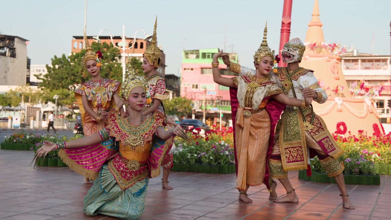 Penampil Asia dengan kostum emas berornamen dan topeng menari di luar ruangan saat cahaya jam emas.
