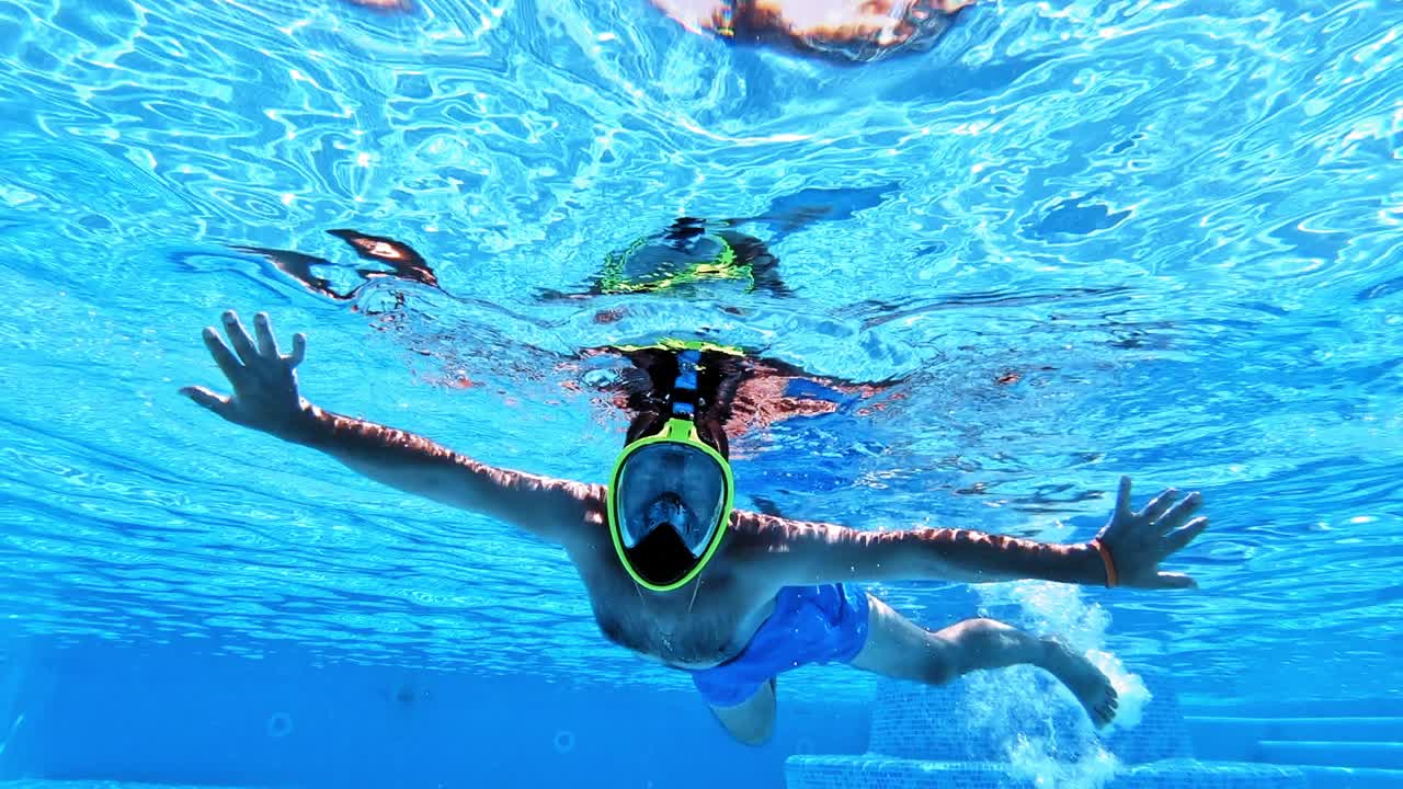 Underwater background of a swimming pool. A man in yellow mask swimming inside the clear blue water of a pool.