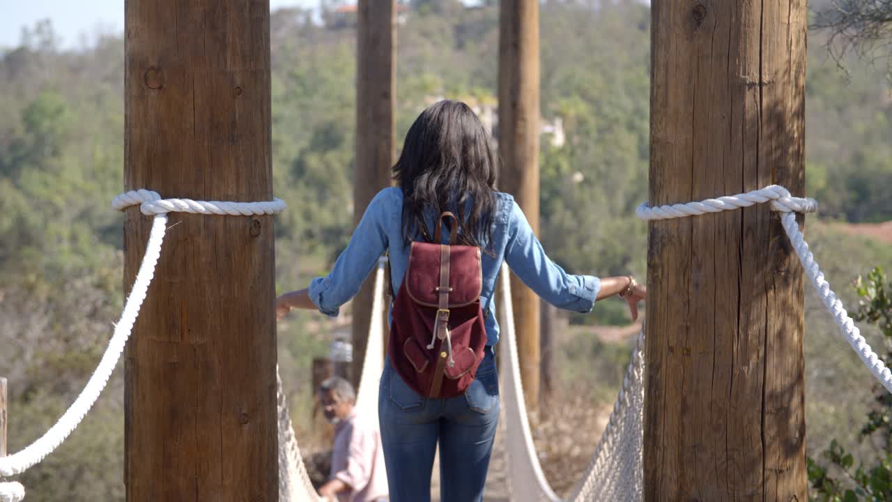 joven negra caminando sobre un puente de cuerda, vista de atrás
