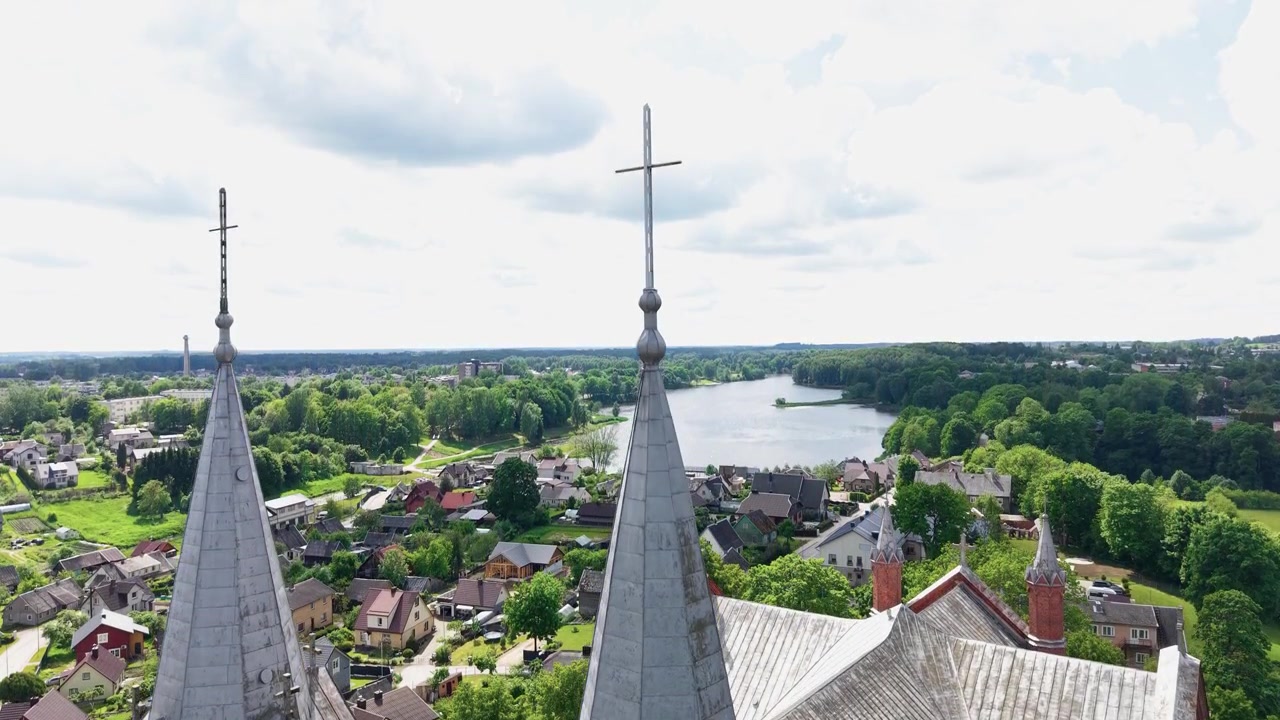 Betagende dronevideo viser den røde murstenskirke Sankt Johannes Døberens Kirke i Plungė, Litauen, med tårnhøje spir, frodigt grønt og fredfyldte hustage, optaget i skarpt dagslys