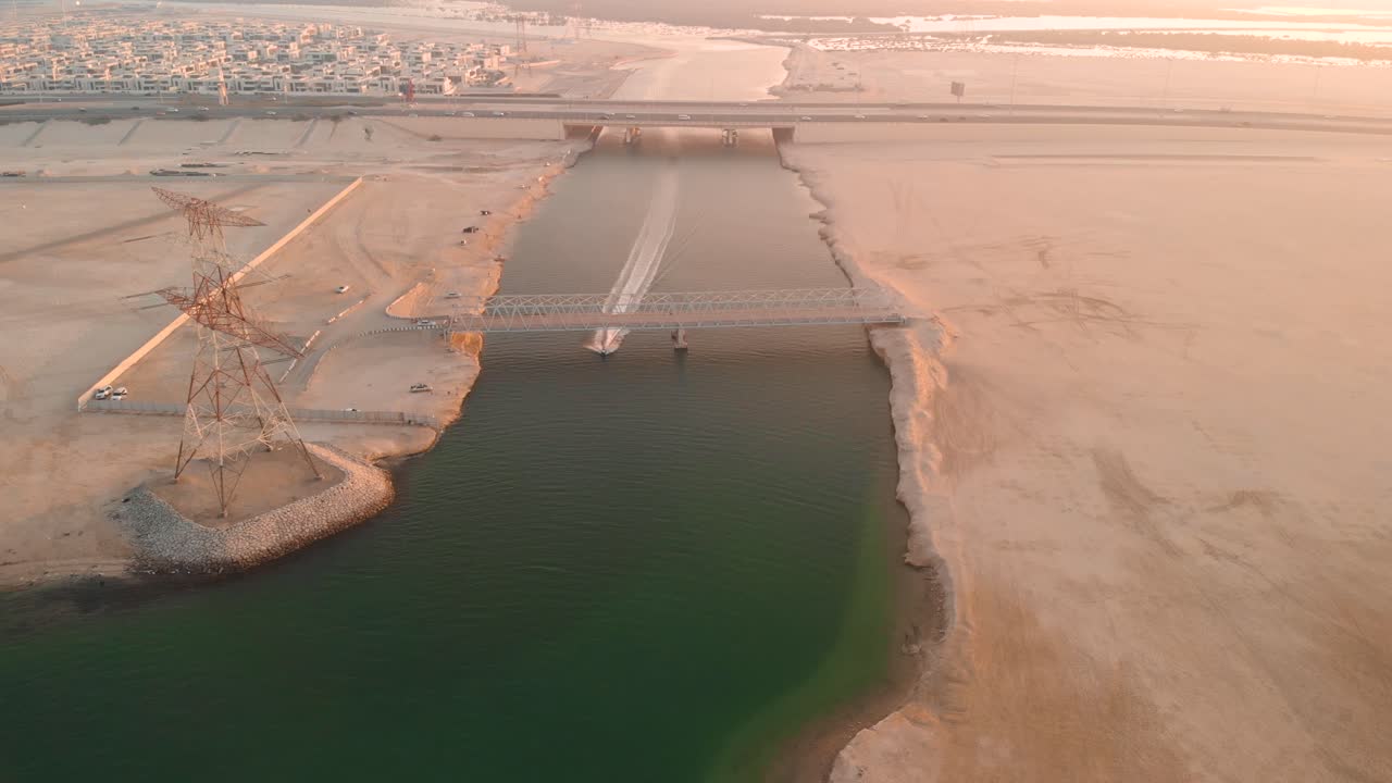 abu dhabi, vista aérea de jetski pasando bajo el puente de metal al atardecer