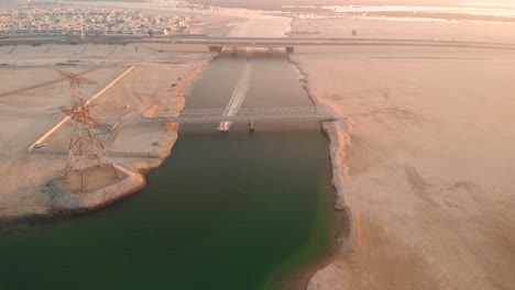 abu dhabi, aerial view of jetski passing under metal bridge at sunset