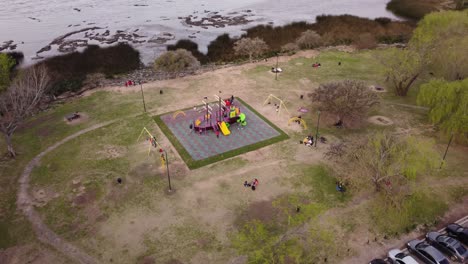 a dynamic orbital aerial footage of kids playing around the children's playground with swings and a sailing ship-designed kiddie slide at the center