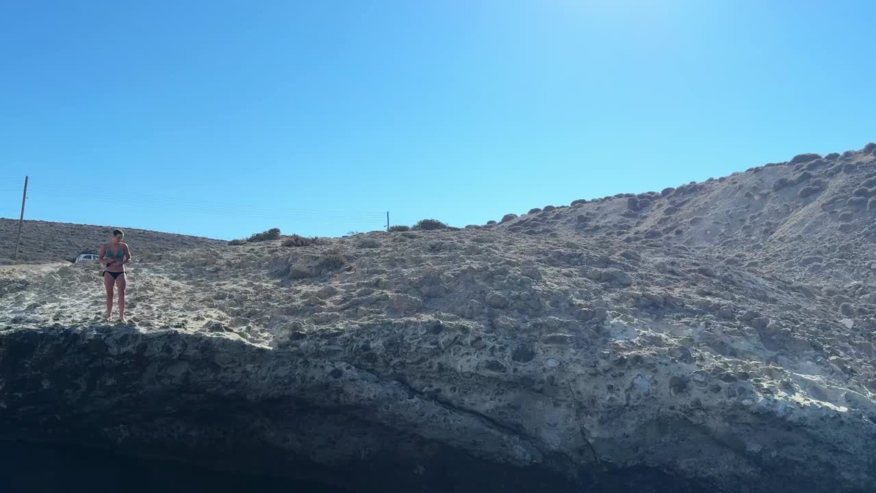 A woman walks along the cliff's edge, preparing to leap into the ocean below.