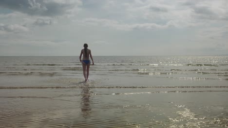 young girl walking out to sea water, warm sunlight scene, slow motion