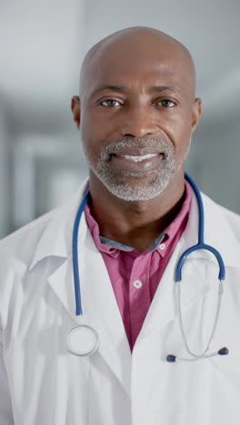 vertical video of portrait of happy african american male doctor wearing stethoscope, slow motion