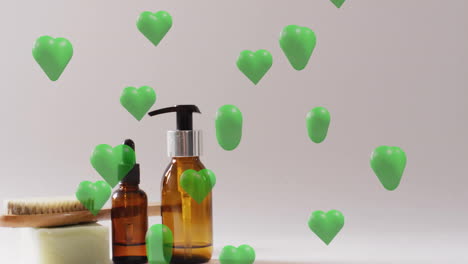 animation of green hearts rising over soap, brush, self care and beauty products on beige background