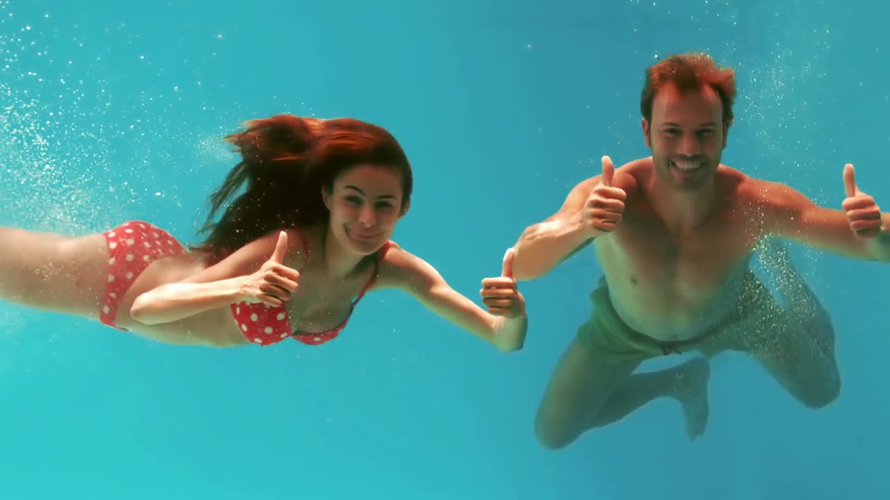 엄지 손가락을 들고 물  ⁇ 에서 헤엄치는 부부