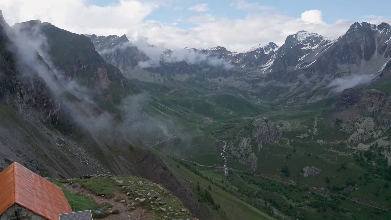 refugio de montaña solitario en medio de picos alpinos nebulosos, un escape sereno en la naturaleza, luz del día, tiro amplio