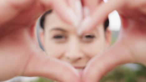 Portrait-of-happy-biracial-woman-making-heart-shape-with-her-hands-standing-on-balcony,-slow-motion