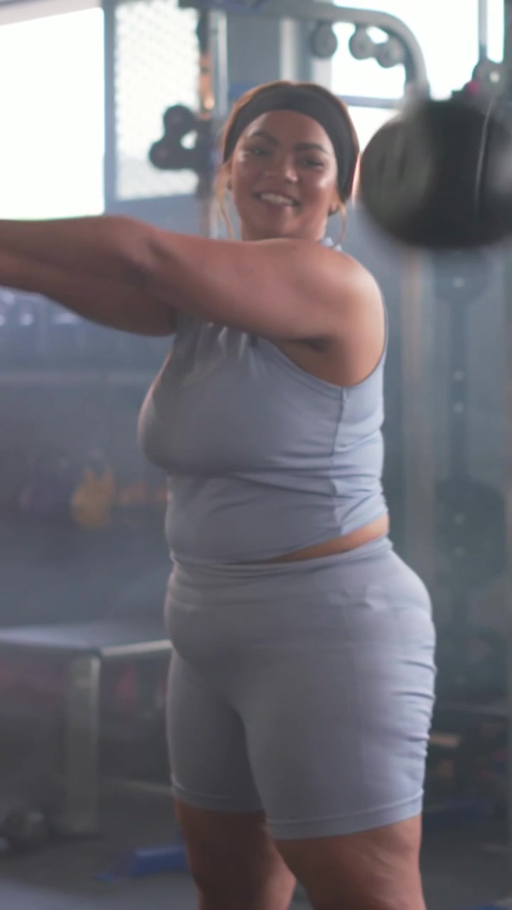 Video verticale: Una donna di mezza età con una canotta blu inizia una serie di esercizi oscillando un kettlebell in palestra, per la forza.