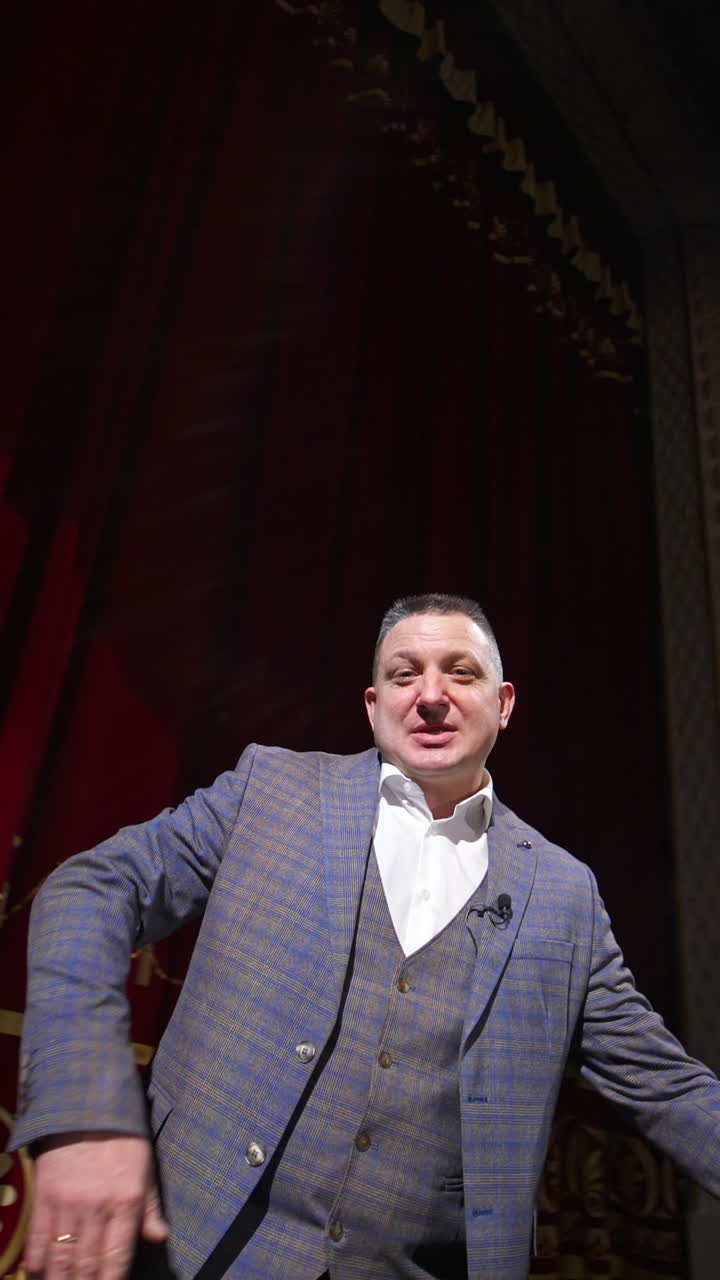 Actor man speaking and dancing on stage. Man in suit on stage in front of empty audience. Orbiting shot. Vertical video