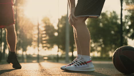 close up of two basketball players stretching their legs in an outdoor baskeball court