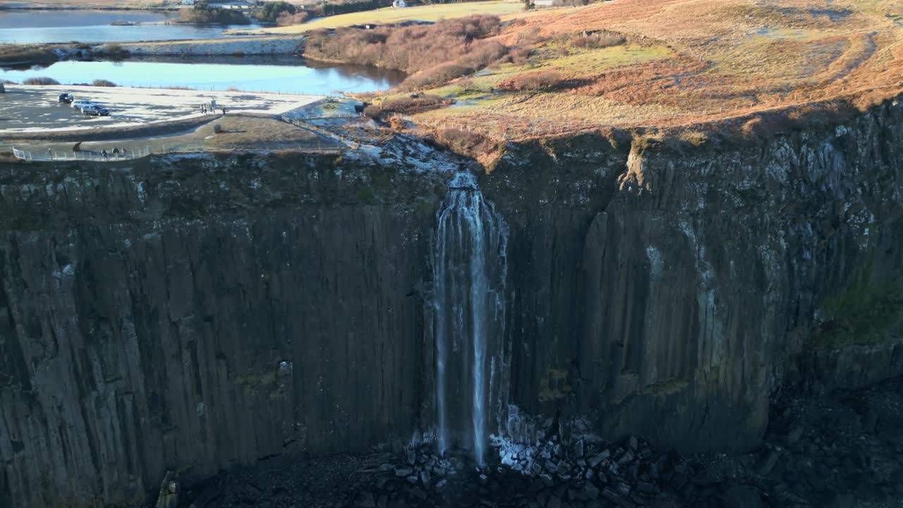 cascada en la sombra en cascada hacia abajo a la playa de piedra helada, temprano en la mañana en invierno con retroceso revela la cima del páramo iluminado por el sol en la cascada de kilt rock, isla de skye, tierras altas occidentales, escocia, reino unido