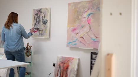 female artist painting figure on a canvas, stood in a home studio