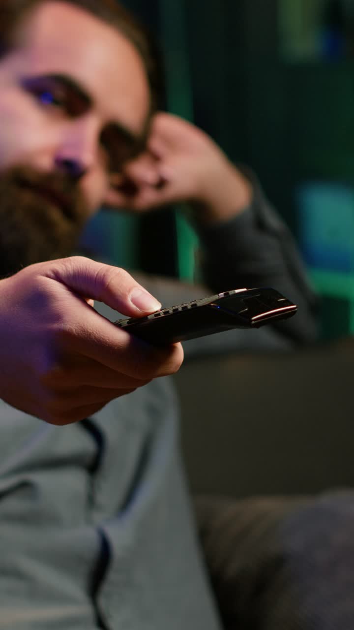 Video verticale. Primo piano di un telecomando usato da un uomo annoiato che fa zapping tra i canali TV.