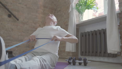 old male using a stretching band and exercising on yoga mat at home 1