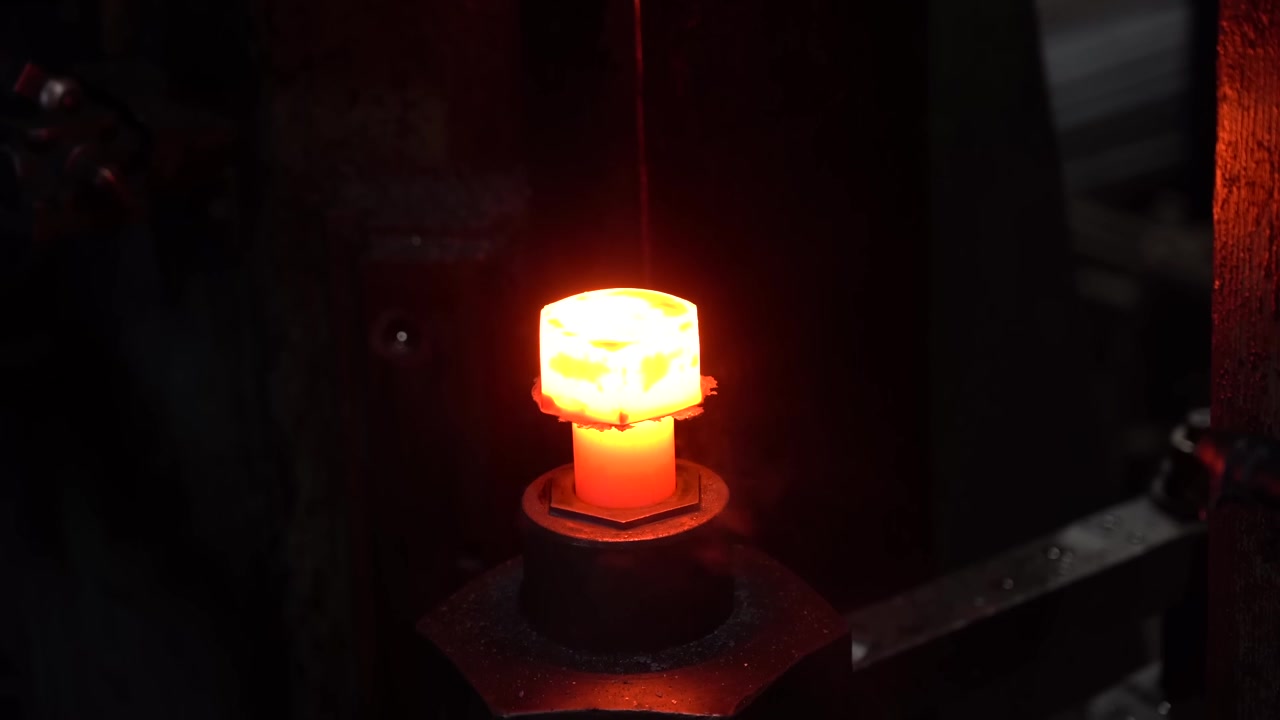 Glowing red hot forged hex bolt head resting on a steel die after forging