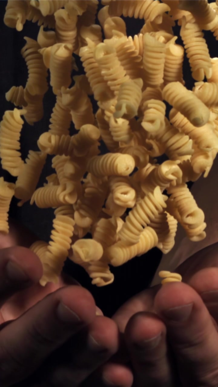 Slow Motion Shot of Dry Fusilli Pasta Falling into Hands