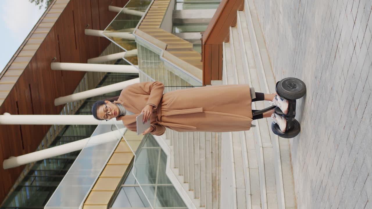 Woman riding a self-balancing scooter while using a tablet in a modern urban environment