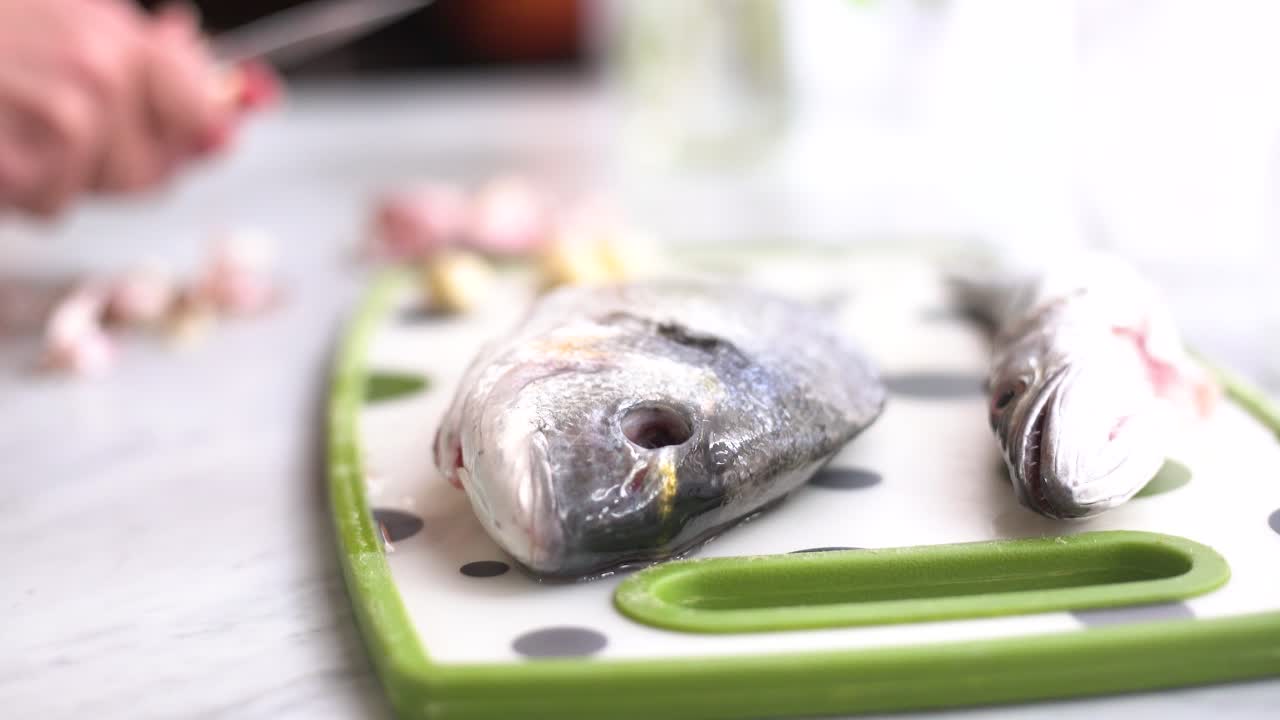 hand peeling garlic next to a sea bream and a whiting on the work surface