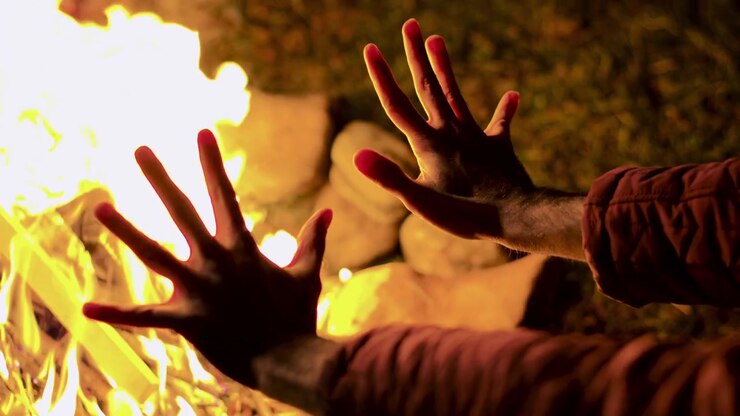 Young man seeks warmth beside an autumn campfire