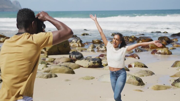 Homme afro-américain prenant sa femme en photo avec un appareil numérique à la plage.