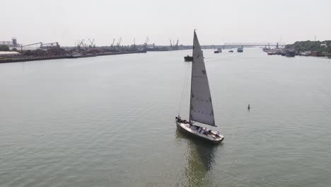 sailing yacht on river with industrial port background