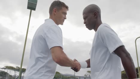 happy diverse male tennis players shaking hands at outdoor tennis court in slow motion