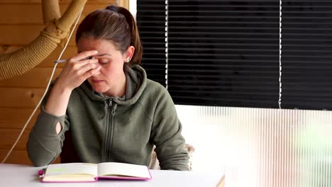 woman sitting at table thinking of ideas to write in notebook, medium shot