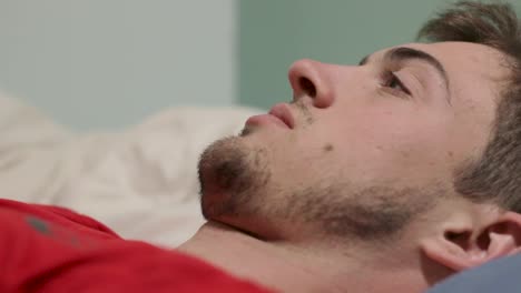 man lying on bed staring in front of him looking concerned