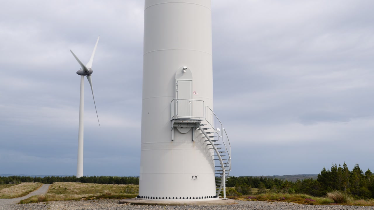 Static shot of a wind turbine foundation with a wind turbine spinning.
