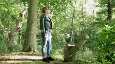 stylish young woman stands next to stump in bright forest, full