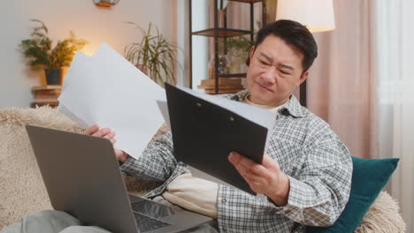 stressed man freelancer feeling worried about financial problem doing paperwork sitting on sofa