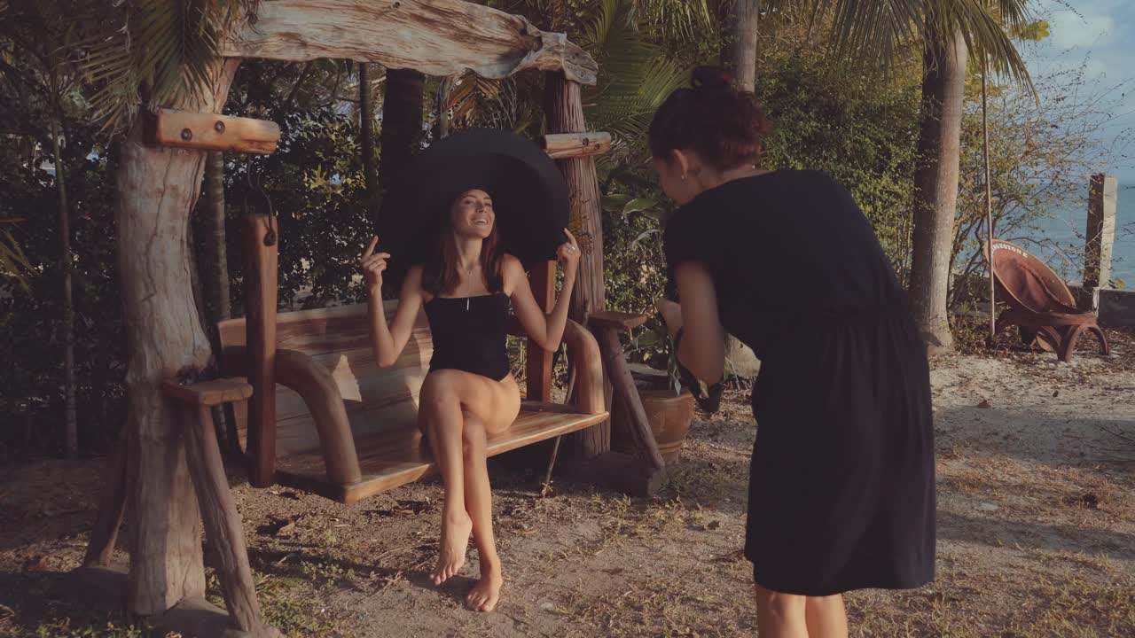 Modella in posa con un grande cappello su un'altalena durante un servizio fotografico all'aperto