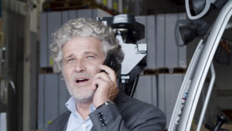 senior businessman standing in warehouse and talking on phone