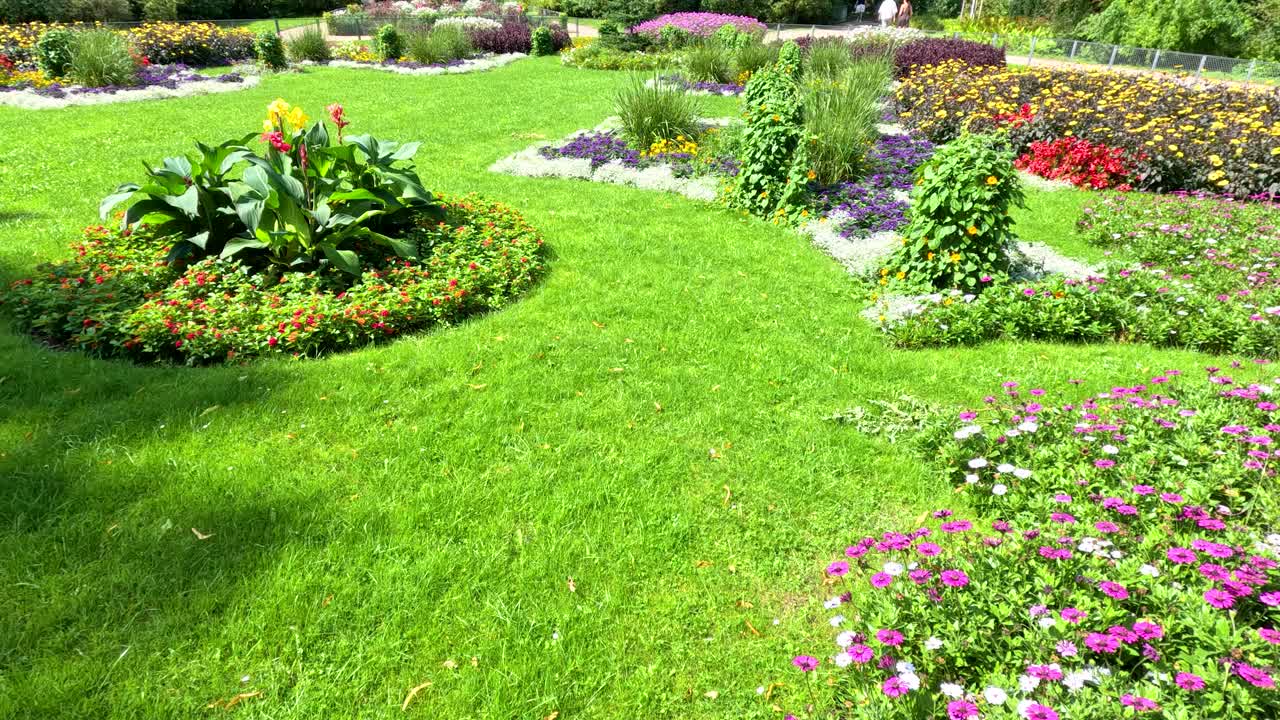 Camera slowly pans over a vibrant urban park in Berlin, highlighting manicured flower beds, lush green grass, and bright natural daylight