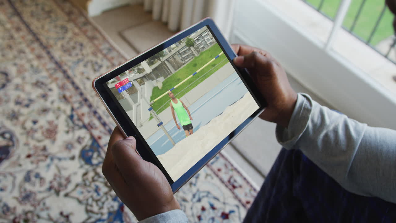 compuesto de un hombre sentado en casa viendo atletismo salto de altura evento en la tableta