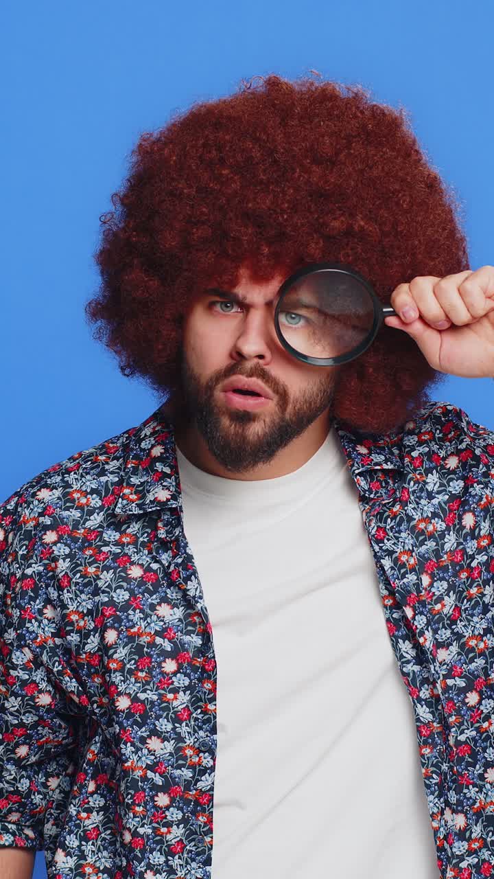 Investigator man holds magnifying glass near face looking at camera with big zoomed eye analyzing