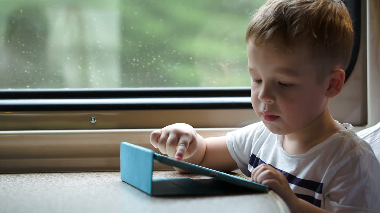 기차에서 패드에서 놀고 있는 소년은 엄마의 도움 없이 이기려고 합니다.