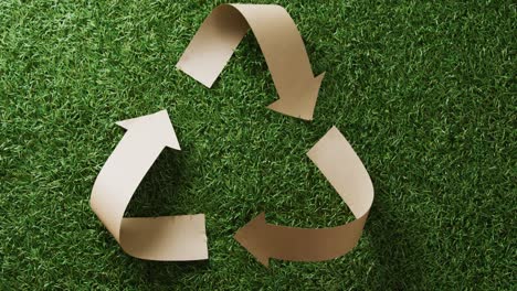 Close-up-of-recycling-symbol-of-paper-arrows-on-grass-background,-with-copy-space