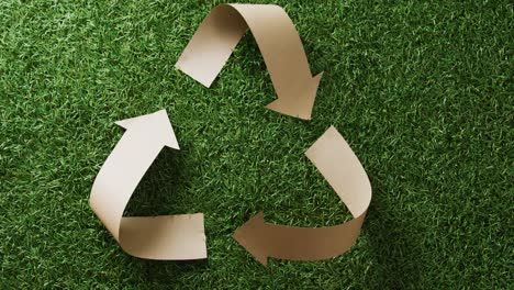 primer plano del símbolo de reciclaje de flechas de papel sobre fondo de hierba, con espacio para copiar